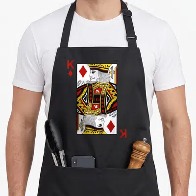 Diamond king apron - Cartoon King of Diamonds playing card with red K and diamond symbols — shown on a black cotton canvas apron against a white background