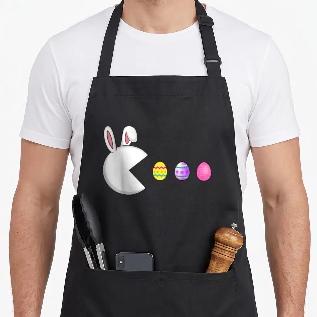 Game easter egg apron - White bunny head facing three yellow purple and pink decorated Easter eggs in cartoon style — shown on a black cotton canvas apron against a white background
