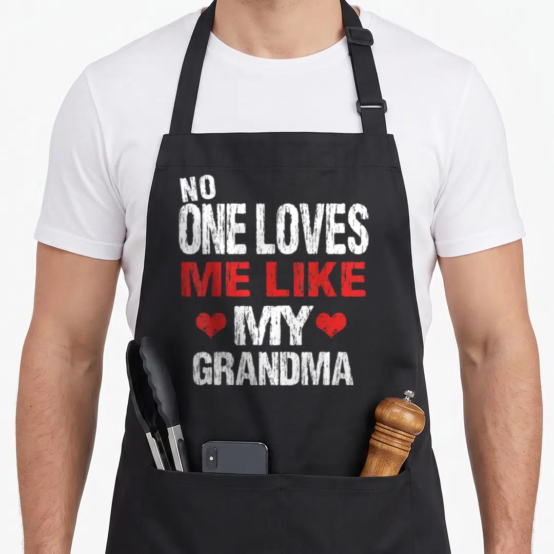 Cute grandmother grandma apron - Stacked white and red distressed text reading No One Loves Me Like My Grandma flanked — shown on a black cotton canvas apron against a white background