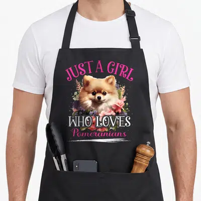 Cool pomeranian dog apron - Realistic Pomeranian head surrounded by pink and green flowers with arched text reading — shown on a black cotton canvas apron against a white background