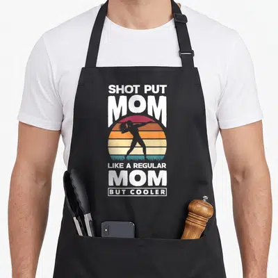 Putter track apron - Retro shot put mom text over striped sunset and grey athlete silhouette — shown on a black cotton canvas apron against a white background