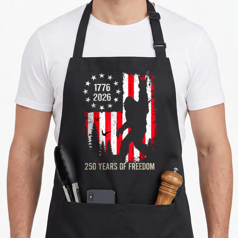 250th anniversary american flag apron - Distressed US flag with bigfoot silhouette and 1776 2026 dates — shown on a black cotton canvas apron against a white background