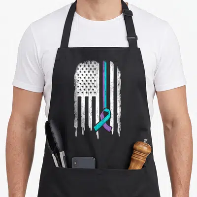 Prevention ribbon apron - Distressed white USA flag with purple and teal awareness ribbon overlapping bottom right — shown on a black cotton canvas apron against a white background