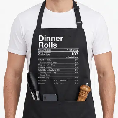 Roll thanksgiving day aprons - White typography nutrition facts label for dinner rolls listing calories and nutrients — shown on a black cotton canvas apron against a white background