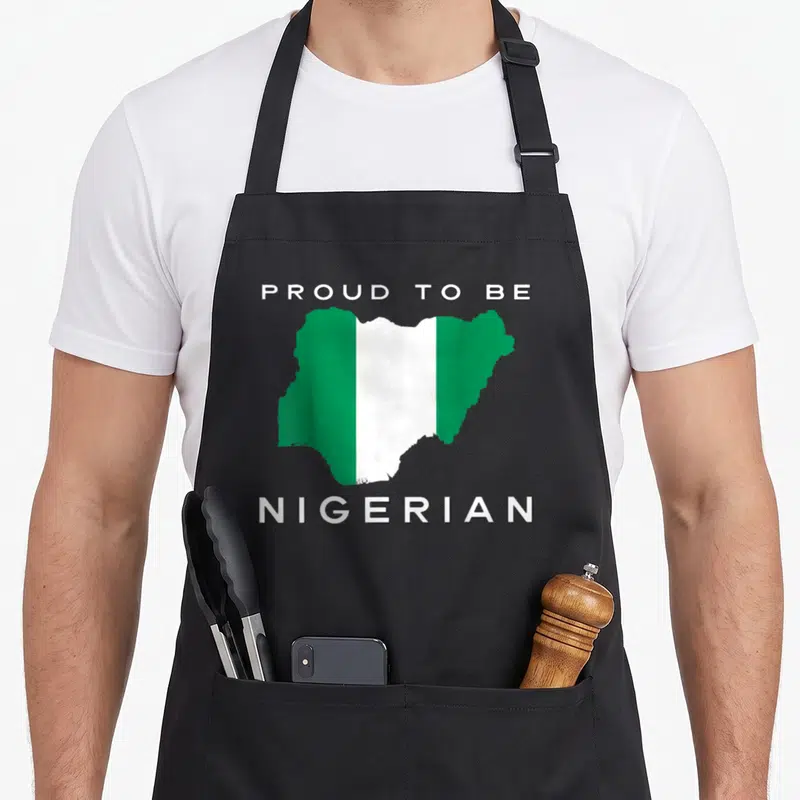 Nigeria patriotic apron - Map of Nigeria in green and white stripes with text PROUD TO BE NIGERIAN above and below — shown on a black cotton canvas apron against a white background