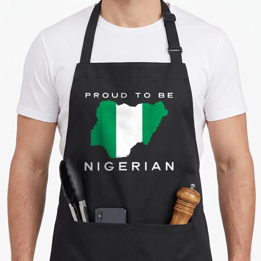 Nigeria patriotic apron - Map of Nigeria in green and white stripes with text PROUD TO BE NIGERIAN above and below — shown on a black cotton canvas apron against a white background