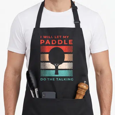 Pong table apron - Grey paddle silhouette over red orange beige teal and grey stripes with bold text — shown on a black cotton canvas apron against a white background