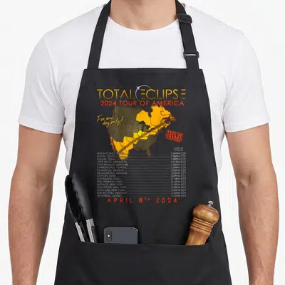 Tour eclipse apron - Map of North America showing yellow totality path with city times and 2024 eclipse date — shown on a black cotton canvas apron against a white background