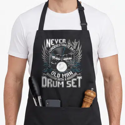 Underestimate black pride apron - Line art of a drum set with wings, flames, and a rock hand symbol surrounded — shown on a black cotton canvas apron against a white background