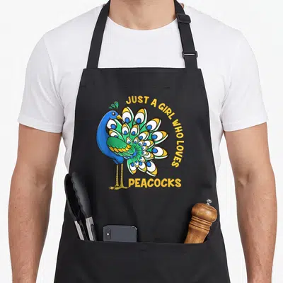 Retro animal apron for grilling - Cartoon peacock in blue and green with yellow text arching over tail feathers — shown on a black cotton canvas apron against a white background