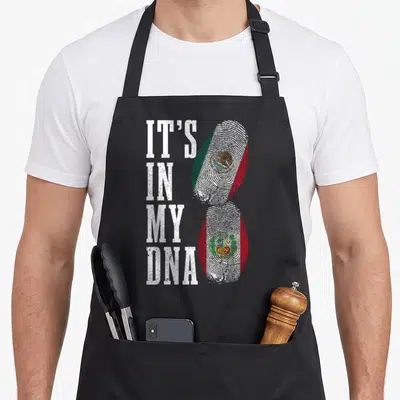 Peru mexico apron - IT'S IN MY DNA text next to two fingerprints filled with Mexican and Peruvian flag colors — shown on a black cotton canvas apron against a white background