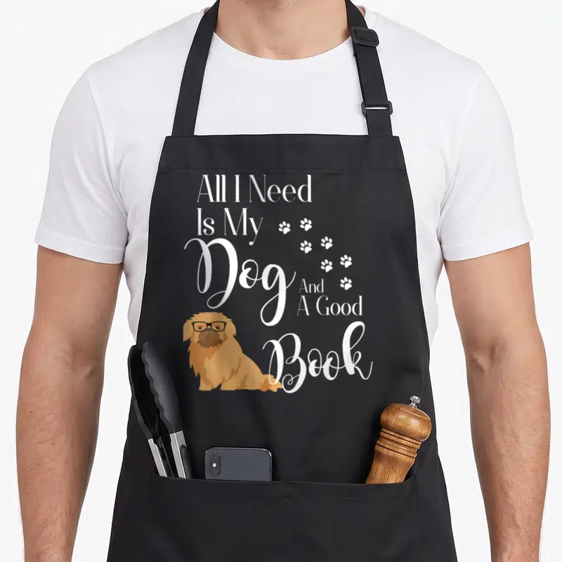 Pekingese reading dog apron - White stacked text All I Need Is My Dog And A Good Book above tan Pekingese with glasses — shown on a black cotton canvas apron against a white background