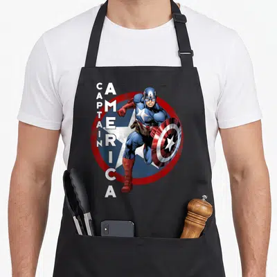Icon captain apron - Realistic hero in blue and red suit holding shield before a large circle with vertical white text — shown on a black cotton canvas apron against a white background