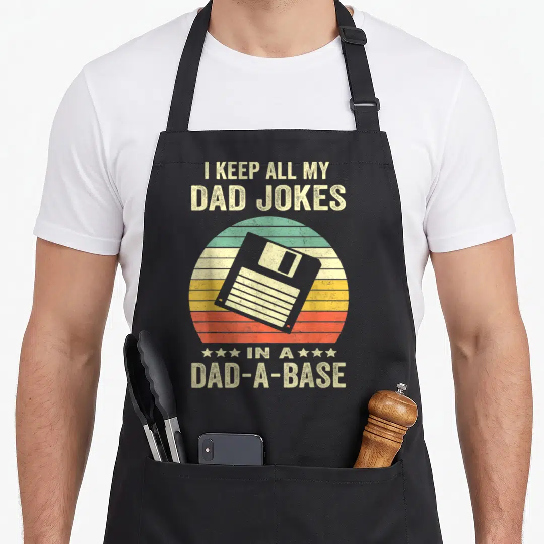 Base father dad joke apron - Grey floppy disk over beige teal yellow orange red striped semi-circle with stacked text — shown on a black cotton canvas apron against a white background