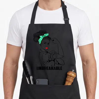 Unbreakable cerebral palsy awareness apron - Cartoon woman flexing arm with Cerebral Palsy Mom tattoo and UNBREAKABLE — shown on a black cotton canvas apron against a white background