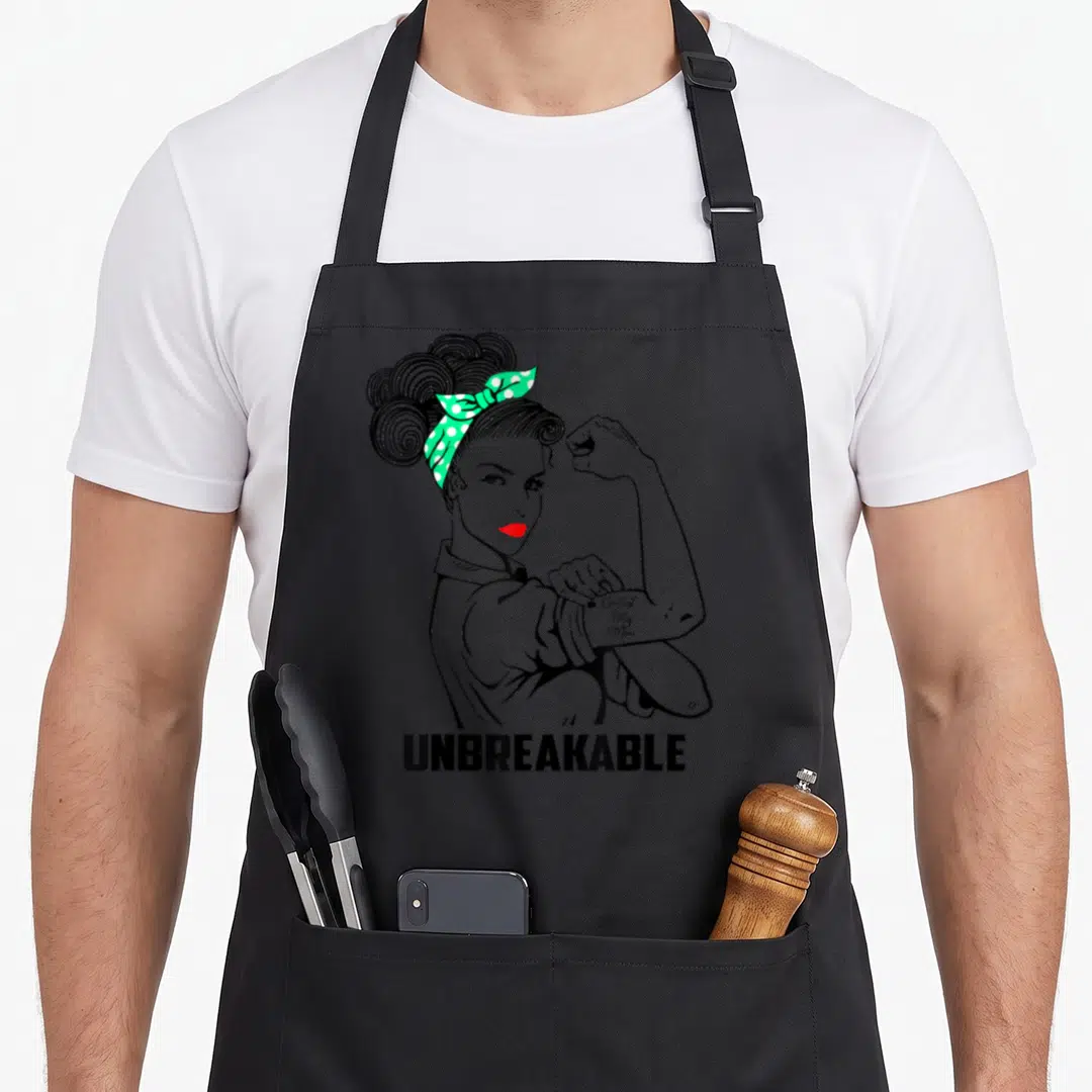 Unbreakable cerebral palsy awareness apron - Cartoon woman flexing arm with Cerebral Palsy Mom tattoo and UNBREAKABLE — shown on a black cotton canvas apron against a white background