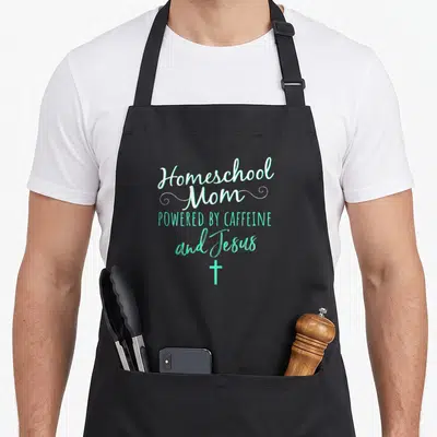 Homeschool christian apron - Stacked white and mint green text reading Homeschool Mom Powered by Caffeine and Jesus — shown on a black cotton canvas apron against a white background