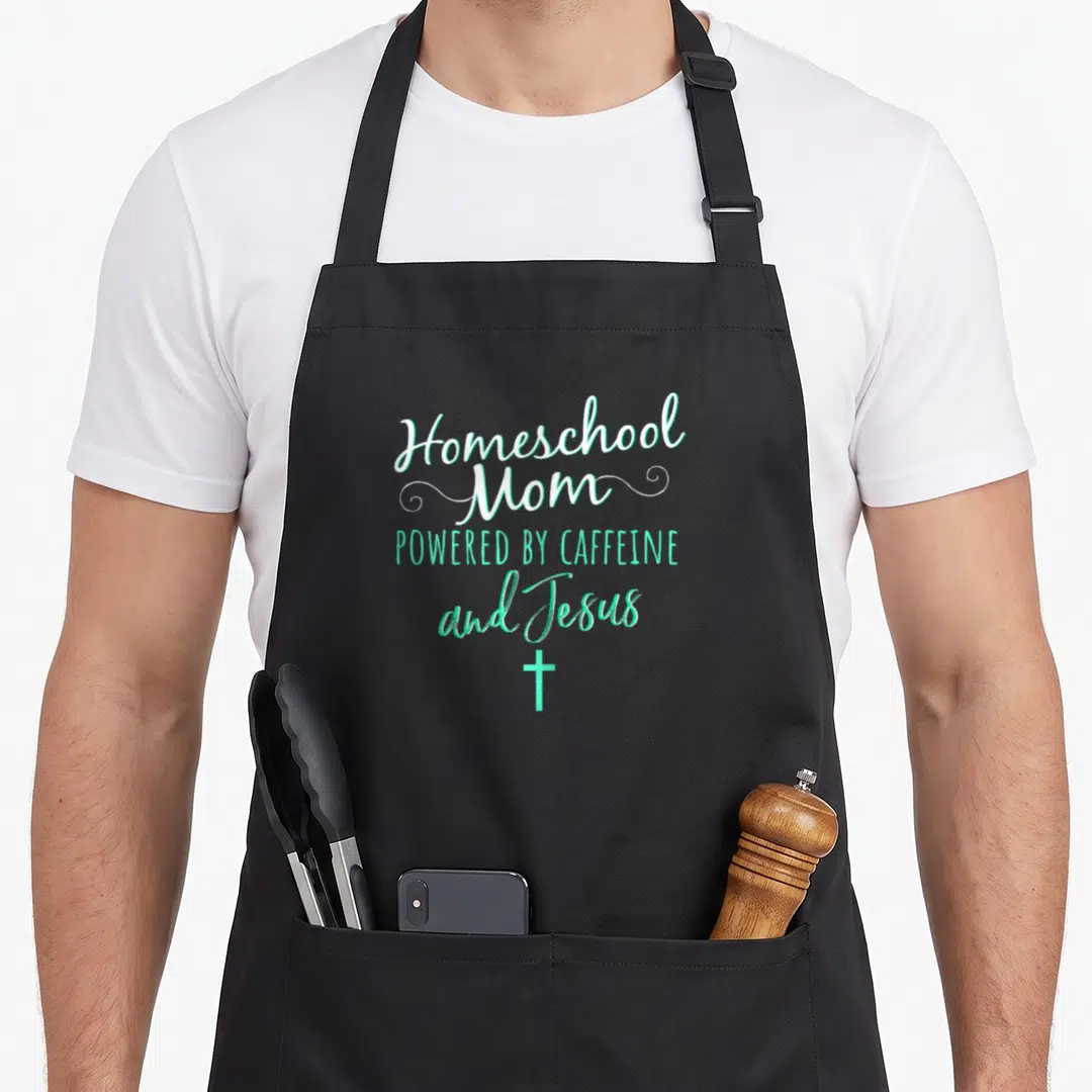 Homeschool christian apron - Stacked white and mint green text reading Homeschool Mom Powered by Caffeine and Jesus — shown on a black cotton canvas apron against a white background