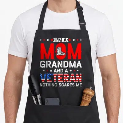 Patriotic grandma apron - Distressed red white blue text with combat boot in O and flag-filled VETERAN — shown on a black cotton canvas apron against a white background