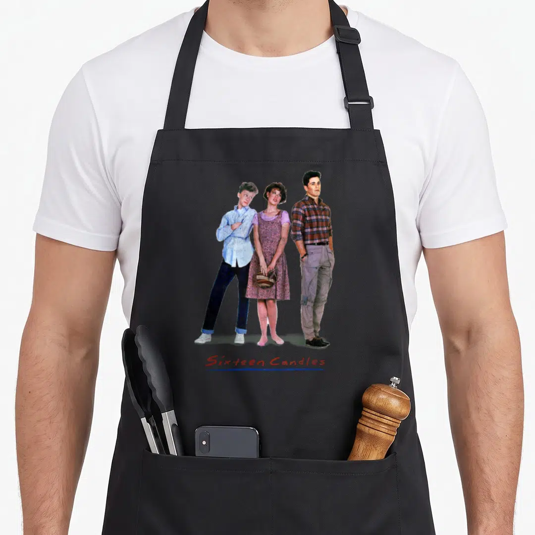 Sixteen movie poster apron - Three people standing side by side above red Sixteen Candles text and blue line — shown on a black cotton canvas apron against a white background
