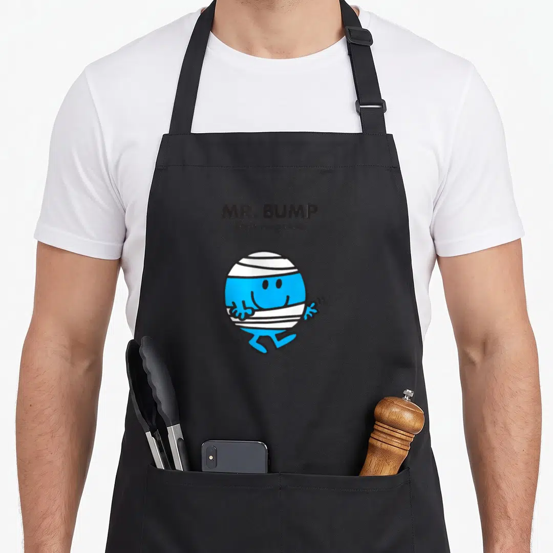 Bump mr apron - MR. BUMP text above a blue round character wrapped in white bandages — shown on a black cotton canvas apron against a white background