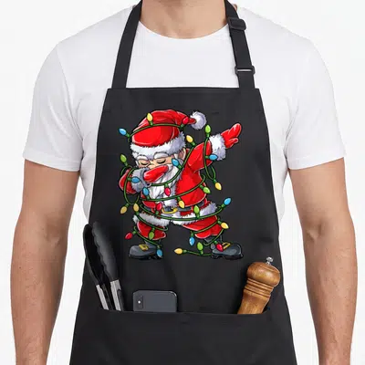 Dabbing christmas tree apron - Santa Claus standing tangled in red white green blue yellow Christmas lights in cartoon — shown on a black cotton canvas apron against a white background