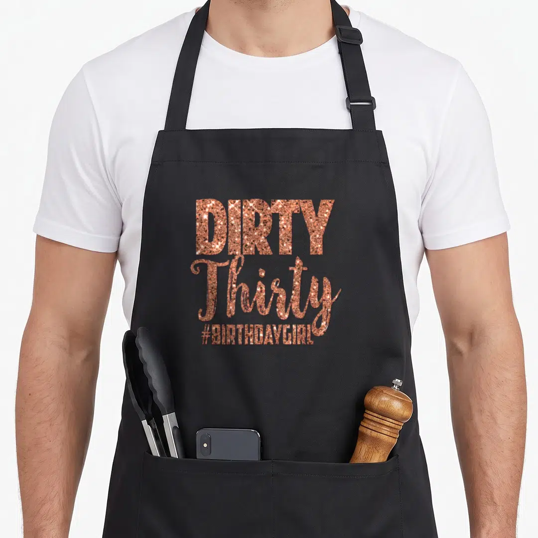 30th funny dirty aprons - Rose gold glitter text reading DIRTY Thirty hashtag BIRTHDAYGIRL in stacked layout — shown on a black cotton canvas apron against a white background