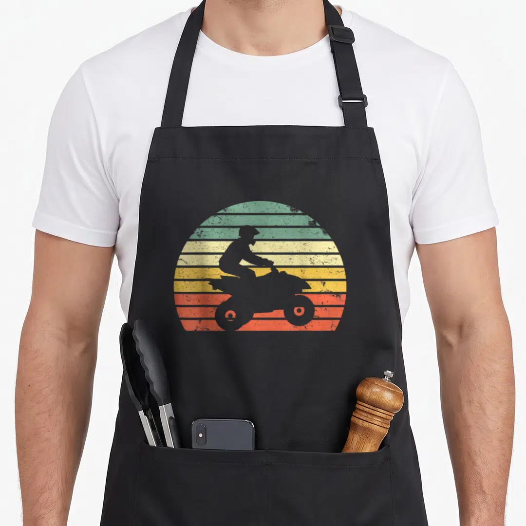 Wheeler atv quotes apron - Grey ATV rider silhouette against green yellow orange red striped sun — shown on a black cotton canvas apron against a white background
