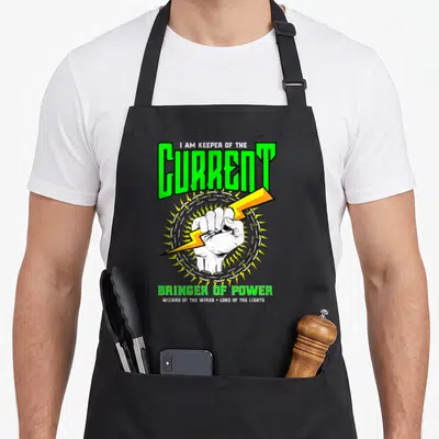 Electrical electrician apron - Fist clutching yellow lightning bolt in silver chain with green text I AM KEEPER — shown on a black cotton canvas apron against a white background