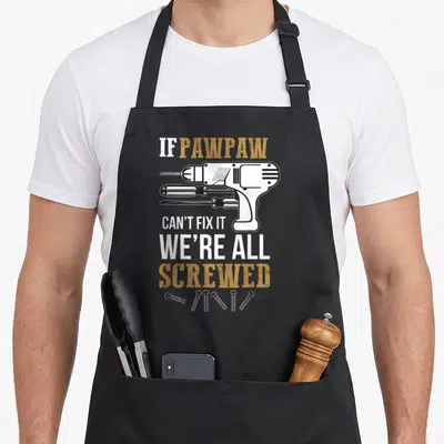 Pawpaw papaya apron - Distressed power drill, two screwdrivers, five screws, and pun text in gold and white — shown on a black cotton canvas apron against a white background