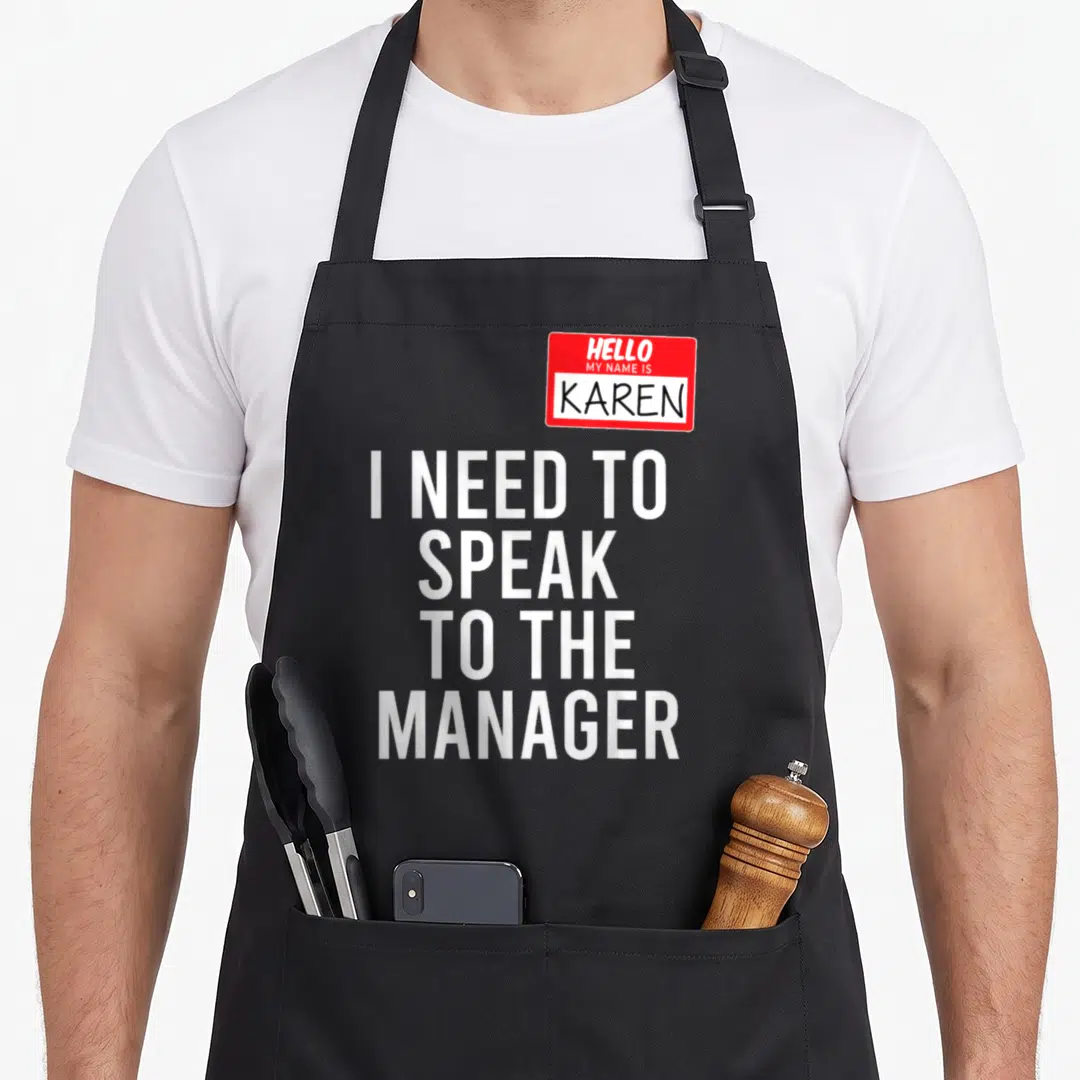 Meme halloween apron - Red name tag with Karen and stacked white text I need to speak to the manager — shown on a black cotton canvas apron against a white background