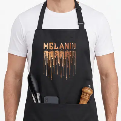 Month pride apron - MELANIN text in tan to brown gradient with vertical paint drips — shown on a black cotton canvas apron against a white background