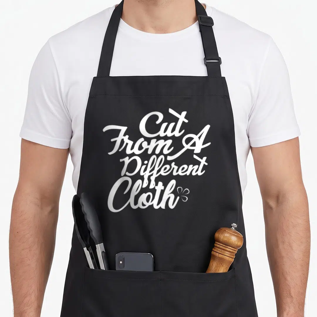 Hop urban apron - White cut from a different cloth text with small flower icon — shown on a black cotton canvas apron against a white background