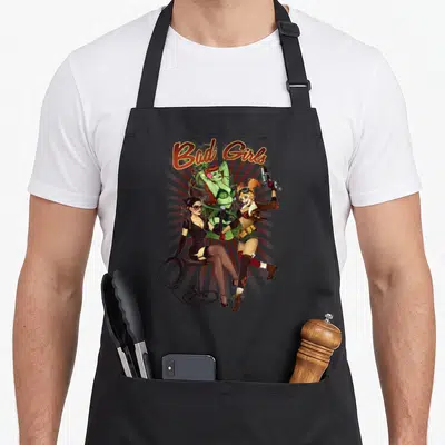 Vintage novelty apron for the kitchen - Three women posing with gun and whip under arched Bad Girls text in cartoon — shown on a black cotton canvas apron against a white background