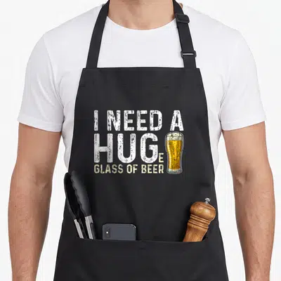 Huge beer brewing apron - Distressed text I Need A Huge Glass Of Beer with yellow beer glass replacing letter E — shown on a black cotton canvas apron against a white background