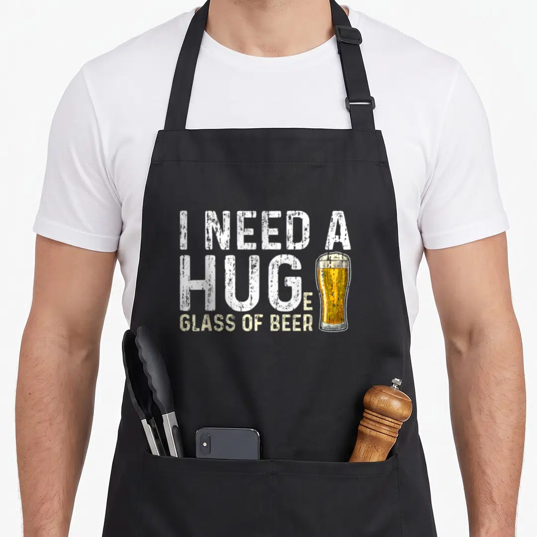 Huge beer brewing apron - Distressed text I Need A Huge Glass Of Beer with yellow beer glass replacing letter E — shown on a black cotton canvas apron against a white background