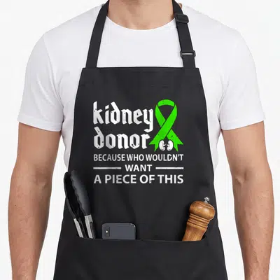 Donor organ apron - Stacked white kidney donor text next to green ribbon containing two small kidney shapes — shown on a black cotton canvas apron against a white background
