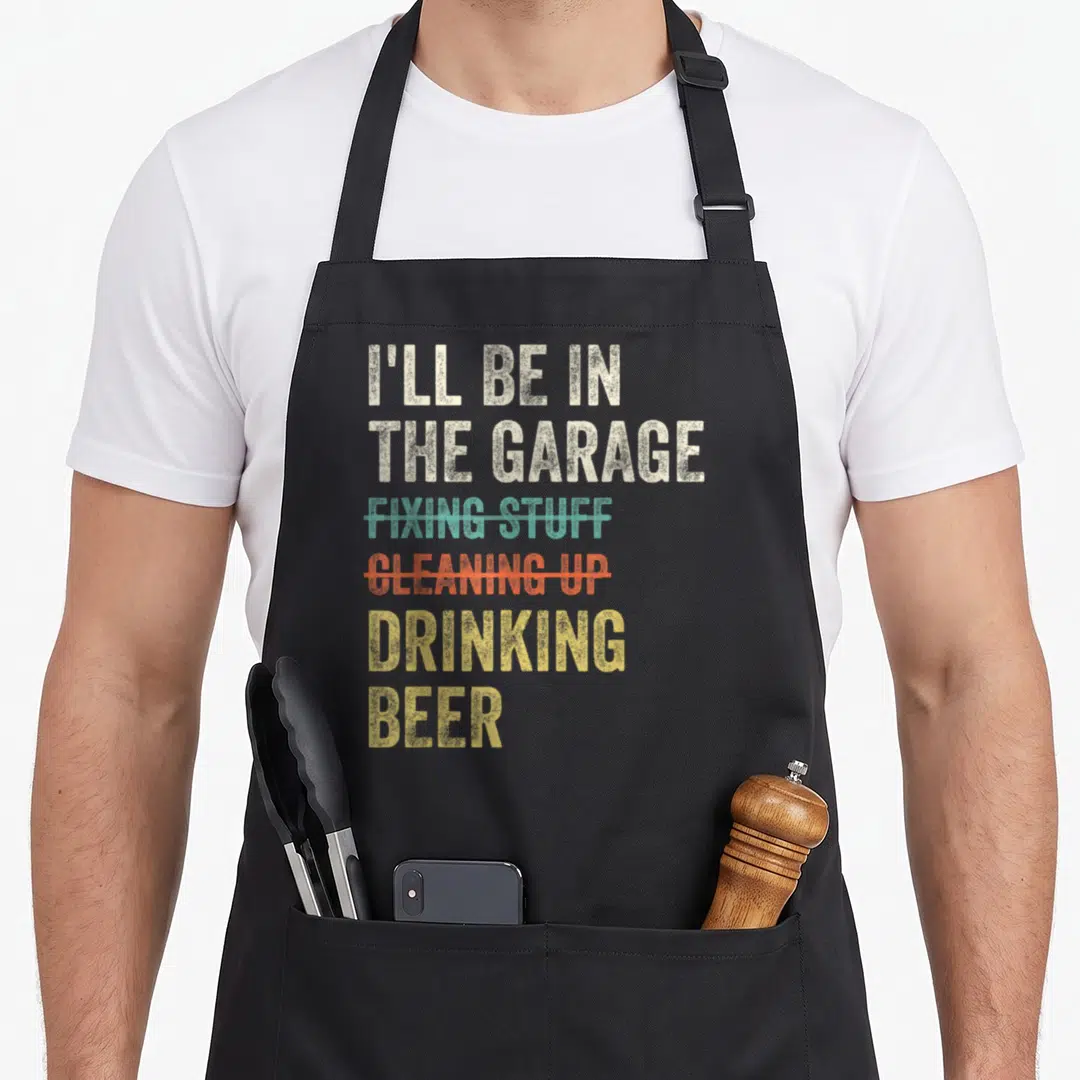 Drinking garage apron - Stacked beige teal orange yellow distressed text with strike-through lines reading I'll be — shown on a black cotton canvas apron against a white background