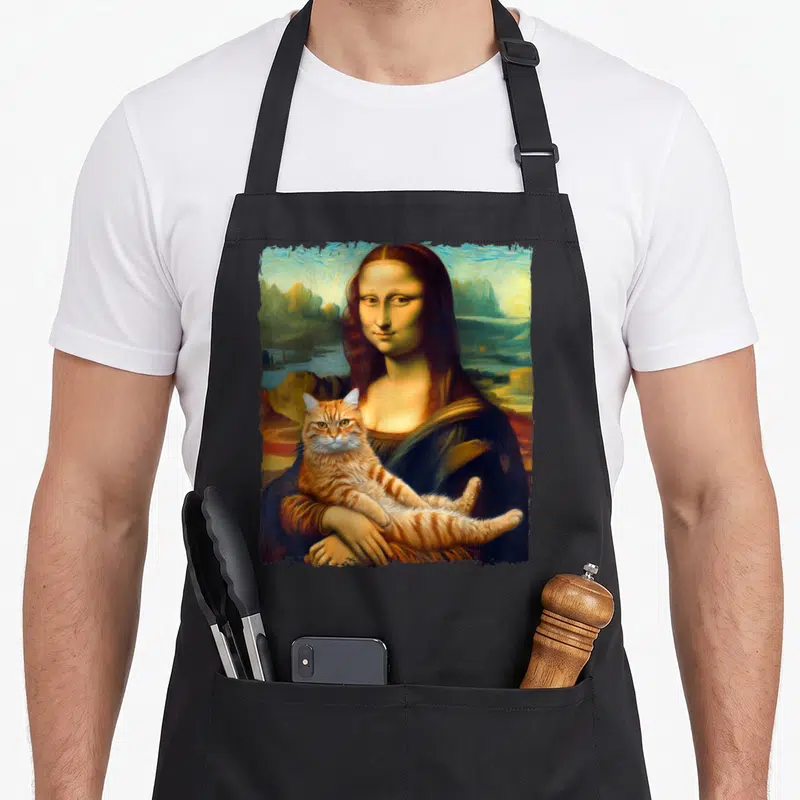 Lisa cat holding apron - Woman holding orange tabby cat in Renaissance portrait style with blue and green background — shown on a black cotton canvas apron against a white background
