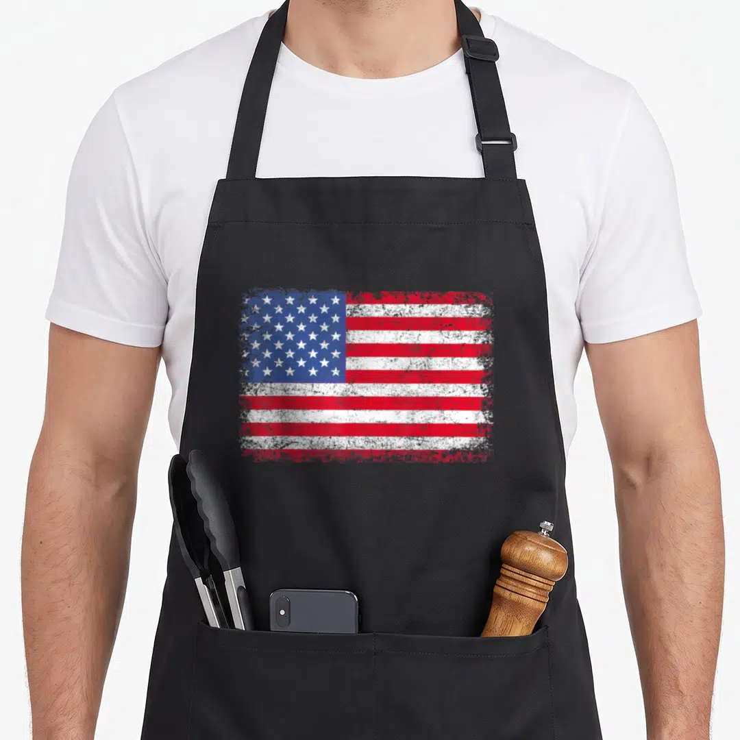 July patriotic aprons - Distressed USA flag in red white blue on black bib apron — shown on a black cotton canvas apron against a white background