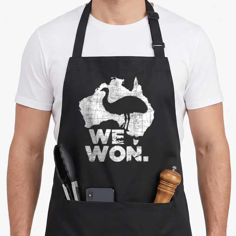 Won australian apron - Grey emu silhouette inside distressed white Australia map with WE WON text below — shown on a black cotton canvas apron against a white background