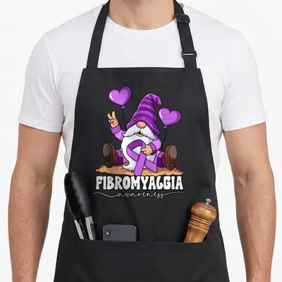 Cool fibromyalgia awareness apron - Cartoon gnome holding purple ribbon and two heart balloons with stacked text below — shown on a black cotton canvas apron against a white background