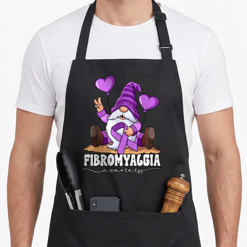 Cool fibromyalgia awareness apron - Cartoon gnome holding purple ribbon and two heart balloons with stacked text below — shown on a black cotton canvas apron against a white background