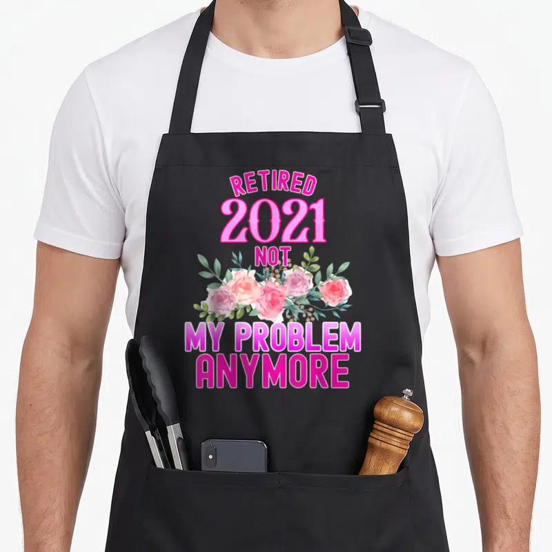 Funny retired retirement apron for grilling - Pink and white flowers with RETIRED 2021 text and green leaves — shown on a black cotton canvas apron against a white background