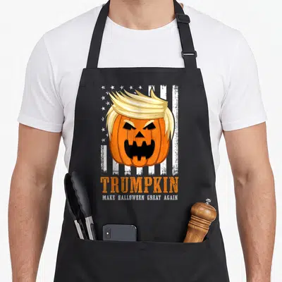 Trumpkin halloween apron - Pumpkin with blonde hair and text TRUMPKIN Make Halloween Great Again — shown on a black cotton canvas apron against a white background