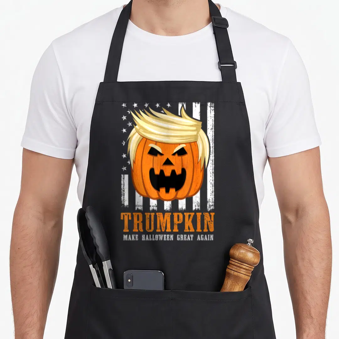 Trumpkin halloween apron - Pumpkin with blonde hair and text TRUMPKIN Make Halloween Great Again — shown on a black cotton canvas apron against a white background