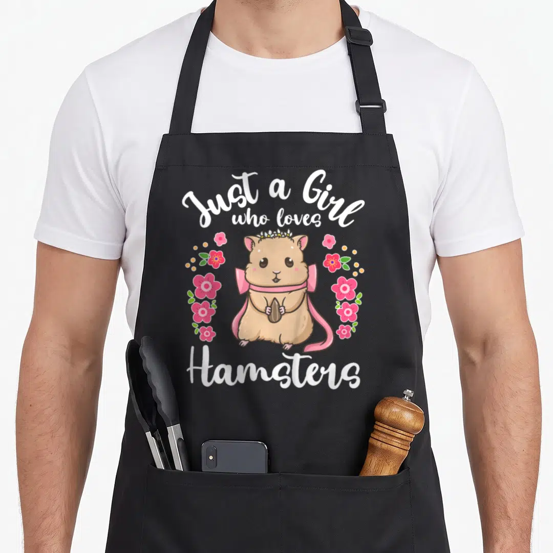 Funny love hamster apron - Tan hamster wearing pink bow and crown holding seed with white text and flowers — shown on a black cotton canvas apron against a white background