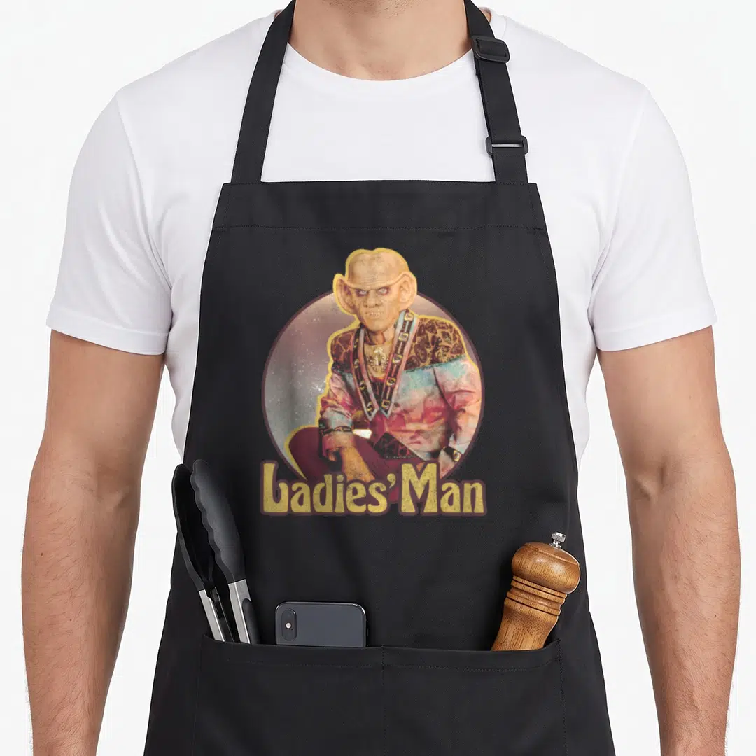 Deep novelty apron - Alien portrait in circle with Ladies' Man text below in yellow and red — shown on a black cotton canvas apron against a white background