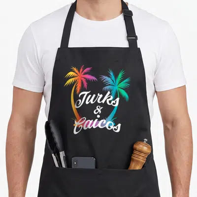 Turk summer aprons - Two gradient palm trees in orange pink blue and green framing white Turks and Caicos script text — shown on a black cotton canvas apron against a white background