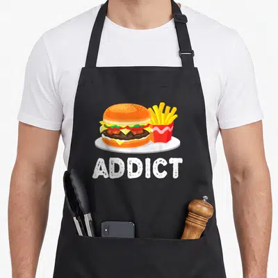 Bacon french apron - Cartoon burger and fries illustration above white ADDICT text — shown on a black cotton canvas apron against a white background